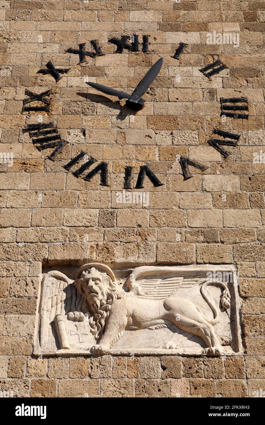 Reloj de la torre de reloj junto a la Iglesia de la Anunciación de la Virgen María en Rodas, Grecia. Un León Veneciano de San Marcos adorna la pared. Foto de stock