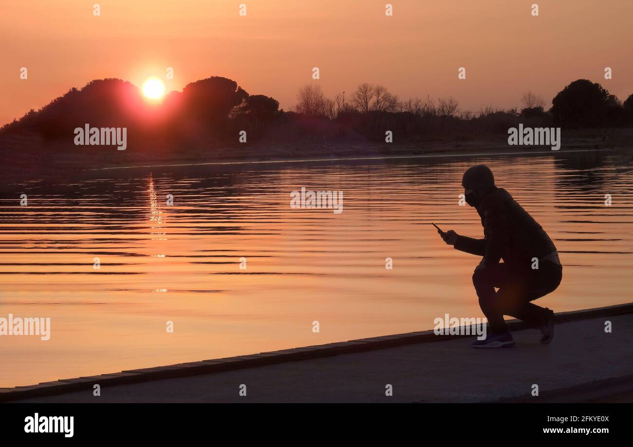 Hombre con smartphone en la mano al atardecer en el río Foto de stock