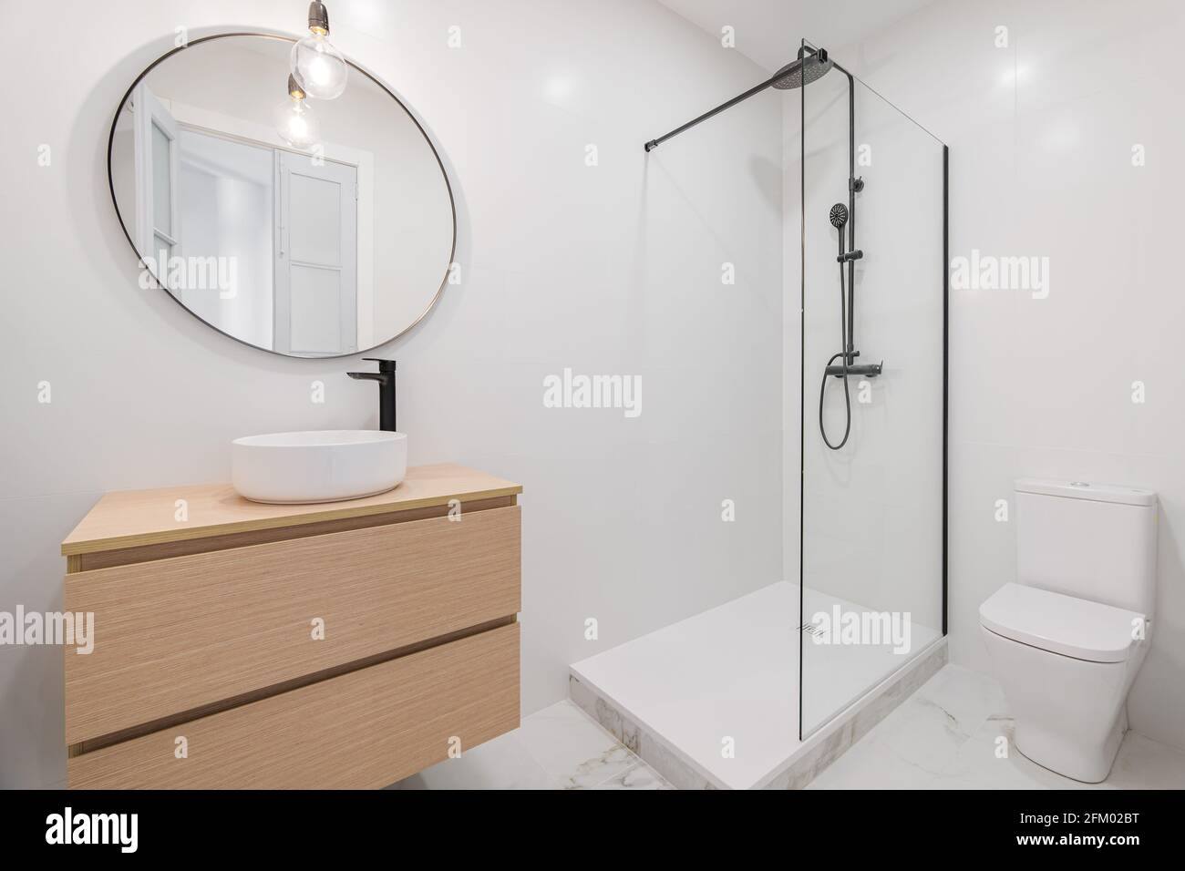 Interior de baño blanco de diseño moderno, con zona de ducha, aseo, suelo  de mármol, muebles de madera y espejo redondo Fotografía de stock - Alamy