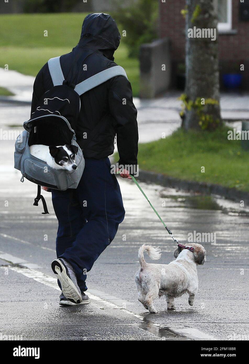 Un hombre lleva a un perro en una mochila mientras camina por otro  siguiendo las fuertes lluvias en Kingswood, Dublín. Fecha de la foto:  Miércoles 5 de mayo de 2021 Fotografía de