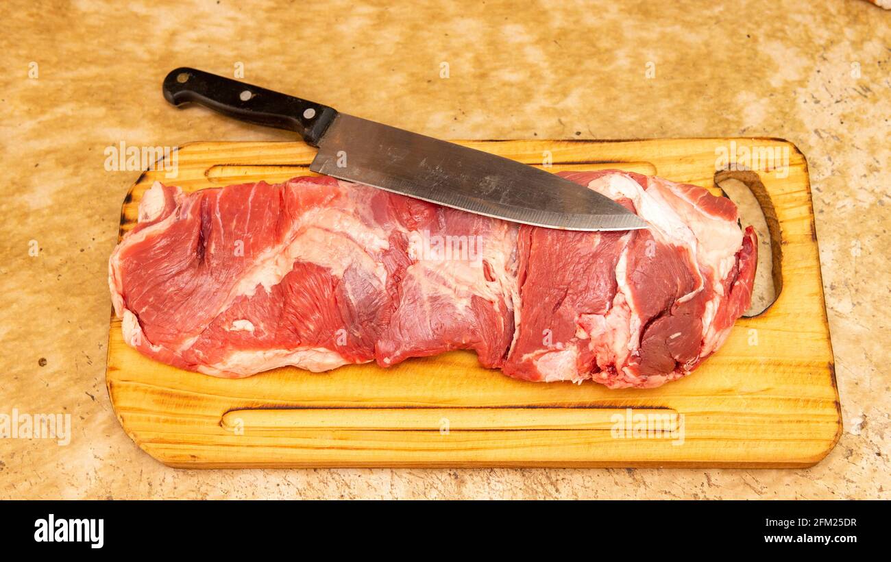 Vista plana de un trozo grande de carne roja cruda en la parte superior de una tabla de corte de madera. Foto de stock