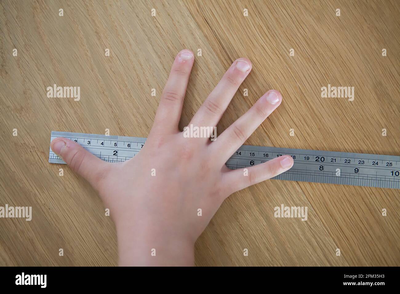 Medir el lapso de mano de un niño en una regla de metal - 18 centímetros Foto de stock