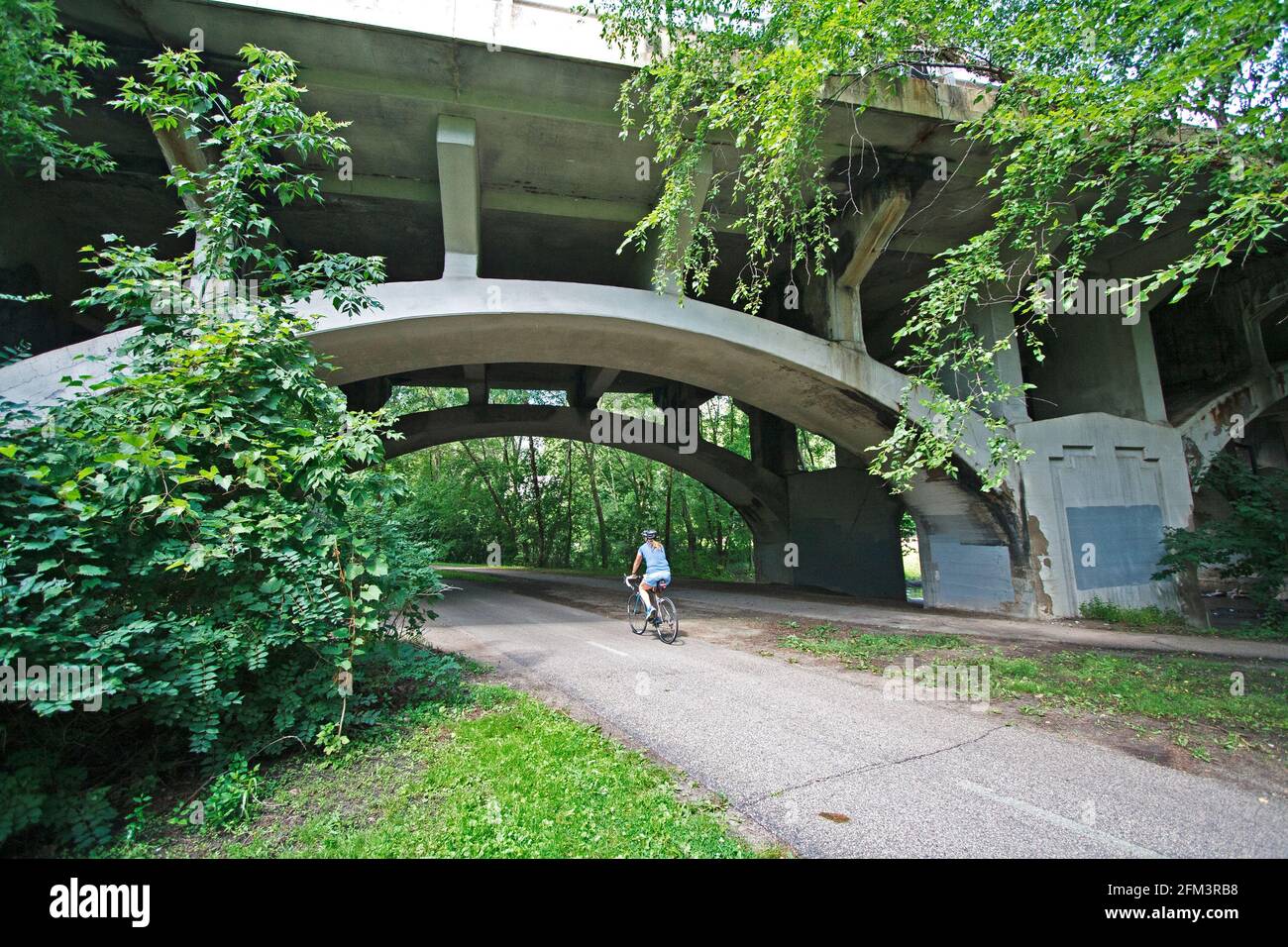 Ciclista que viaja a lo largo de la ruta regional Minnehaha Parkway pasando bajo el arco del puente Nicollet Avenue. Minneapolis Minnesota MN Estados Unidos Foto de stock