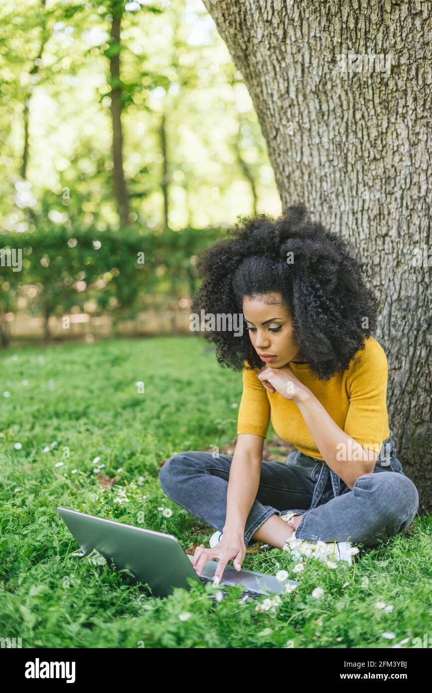 Mujer afro hermosa mecanografiando en un ordenador portátil en un jardín. Foto de stock