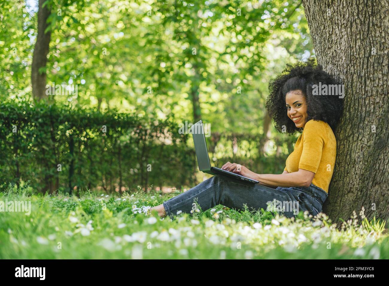 Mujer afro hermosa y feliz mecanografiando en un ordenador portátil en un jardín. Foto de stock