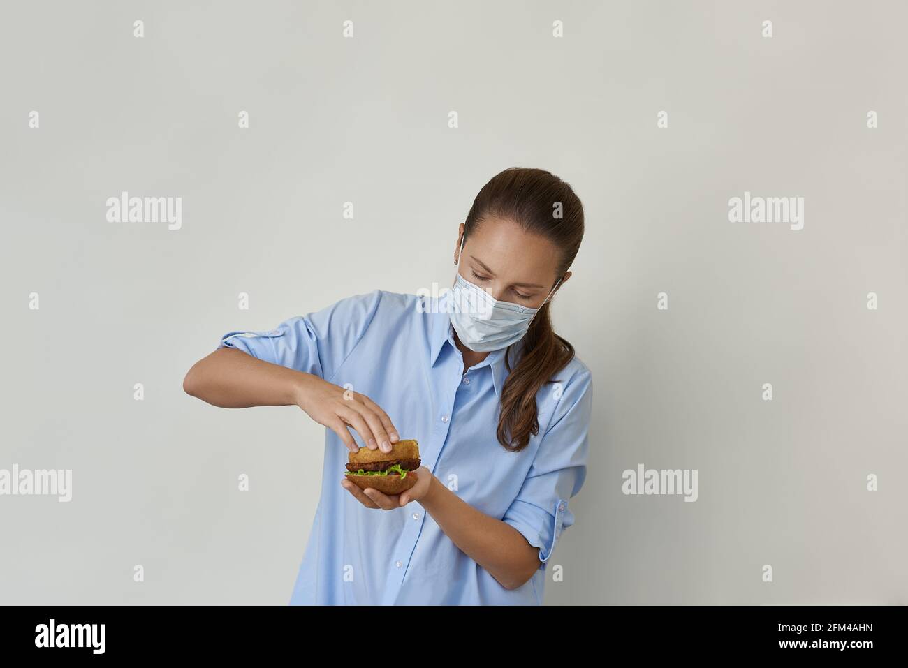 Hermosa mujer joven cocinando hamburguesa vegana en máscara protectora Foto de stock