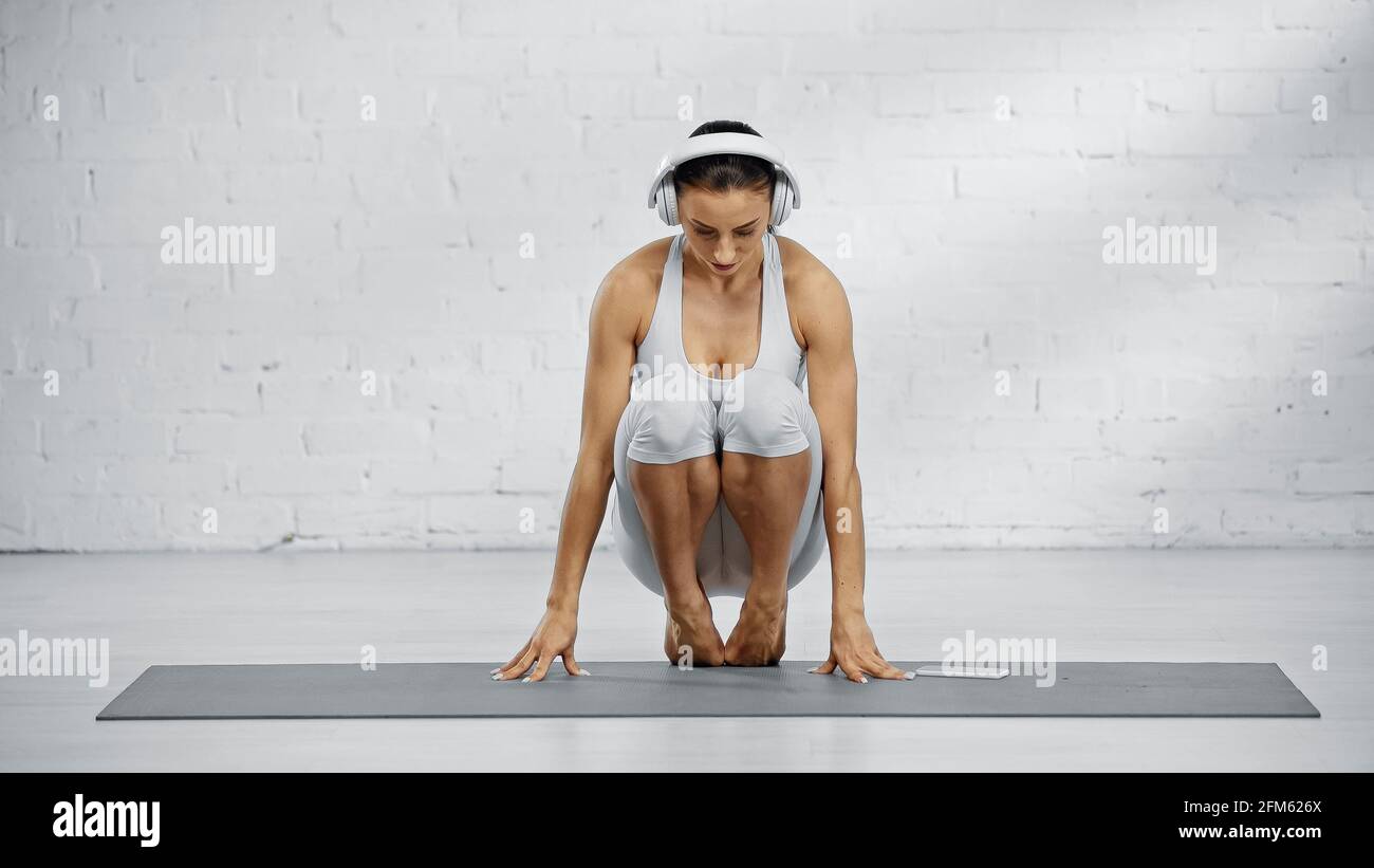 Mujer descalzo en auriculares practicando yoga cerca de smartphone en yoga estera Foto de stock