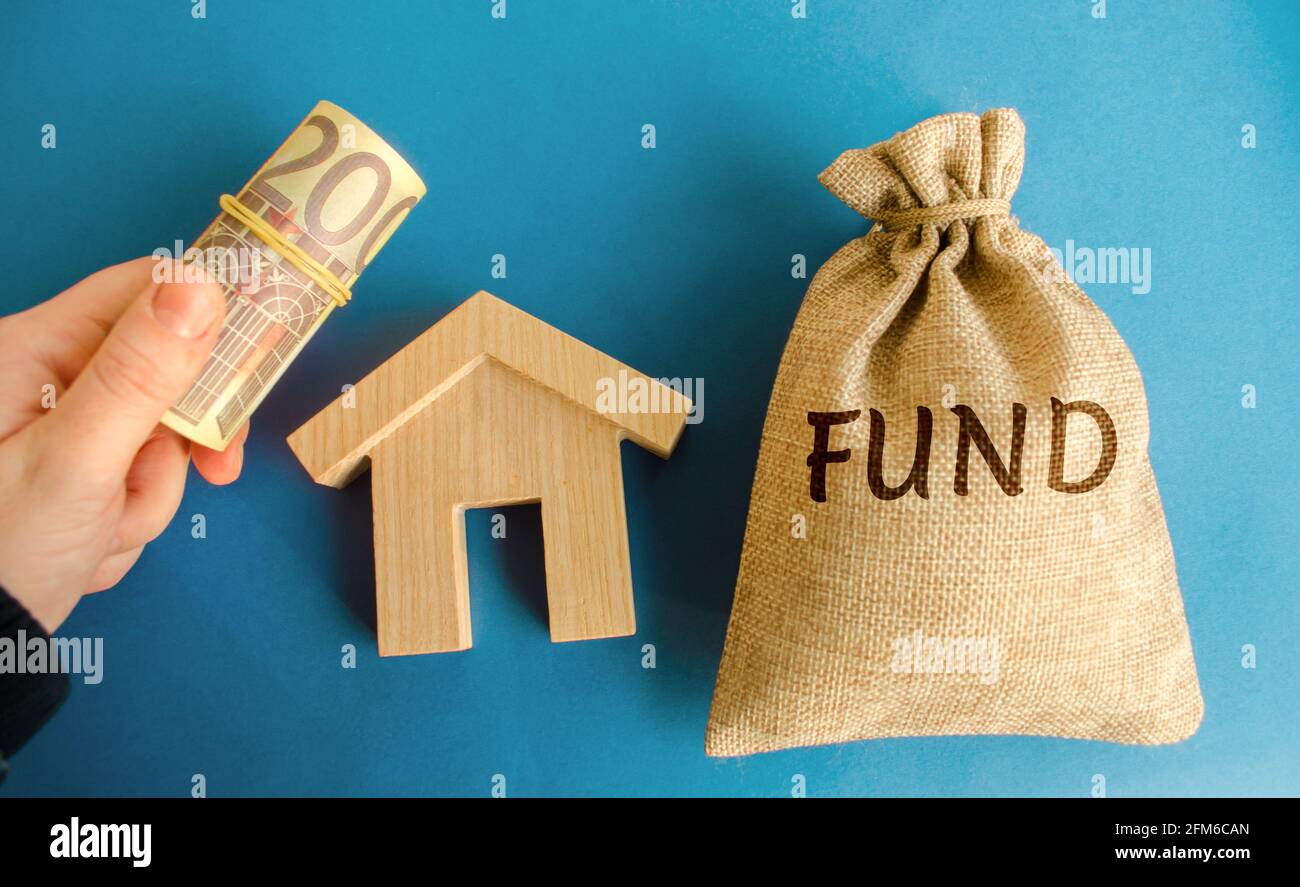 Bolsa de dinero con la palabra Fondo, casa de madera y billetes de euros en la mano. Concepto de inversión inmobiliaria. Proyectos, construcción y explotación inmobiliaria Foto de stock