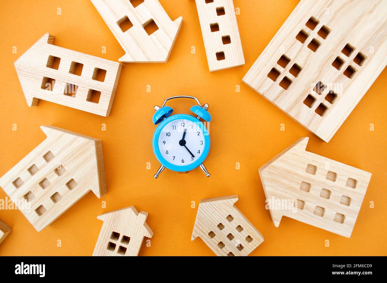Un reloj despertador azul y muchas casas de madera alrededor. Concepto de hipoteca y préstamo. Bienes raíces y riesgos. Seguro de propiedad. Crédito. Pago de impuestos. Utilidades Foto de stock