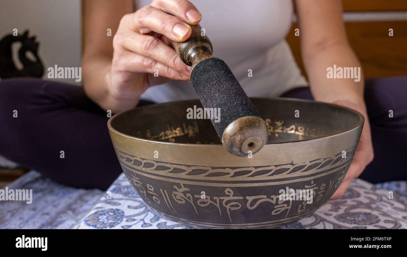 La mujer juega en un tazón de canto decorado con señales tradicionales del mantra budista 'Alabanza a la joya en el loto' para conseguir calma, meditar, escuchar. Foto de stock