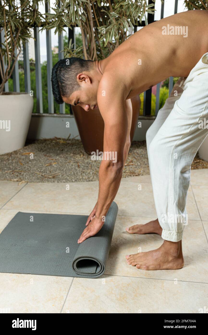 Hombre practicando yoga desenrollando su estera. Foto de stock