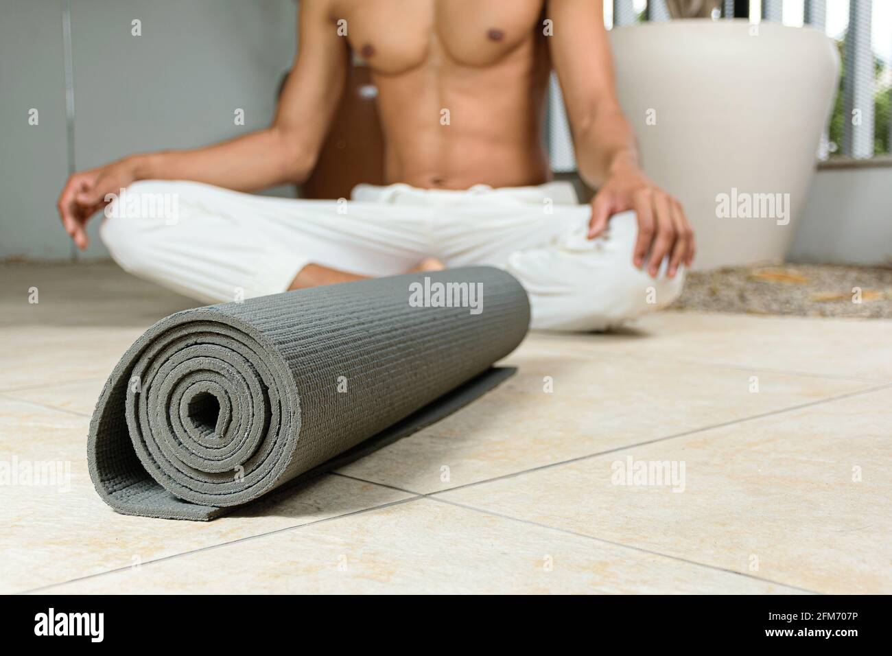 Esterilla de yoga rizado. En el fondo desenfocado, practicante de yoga sentado. Foto de stock