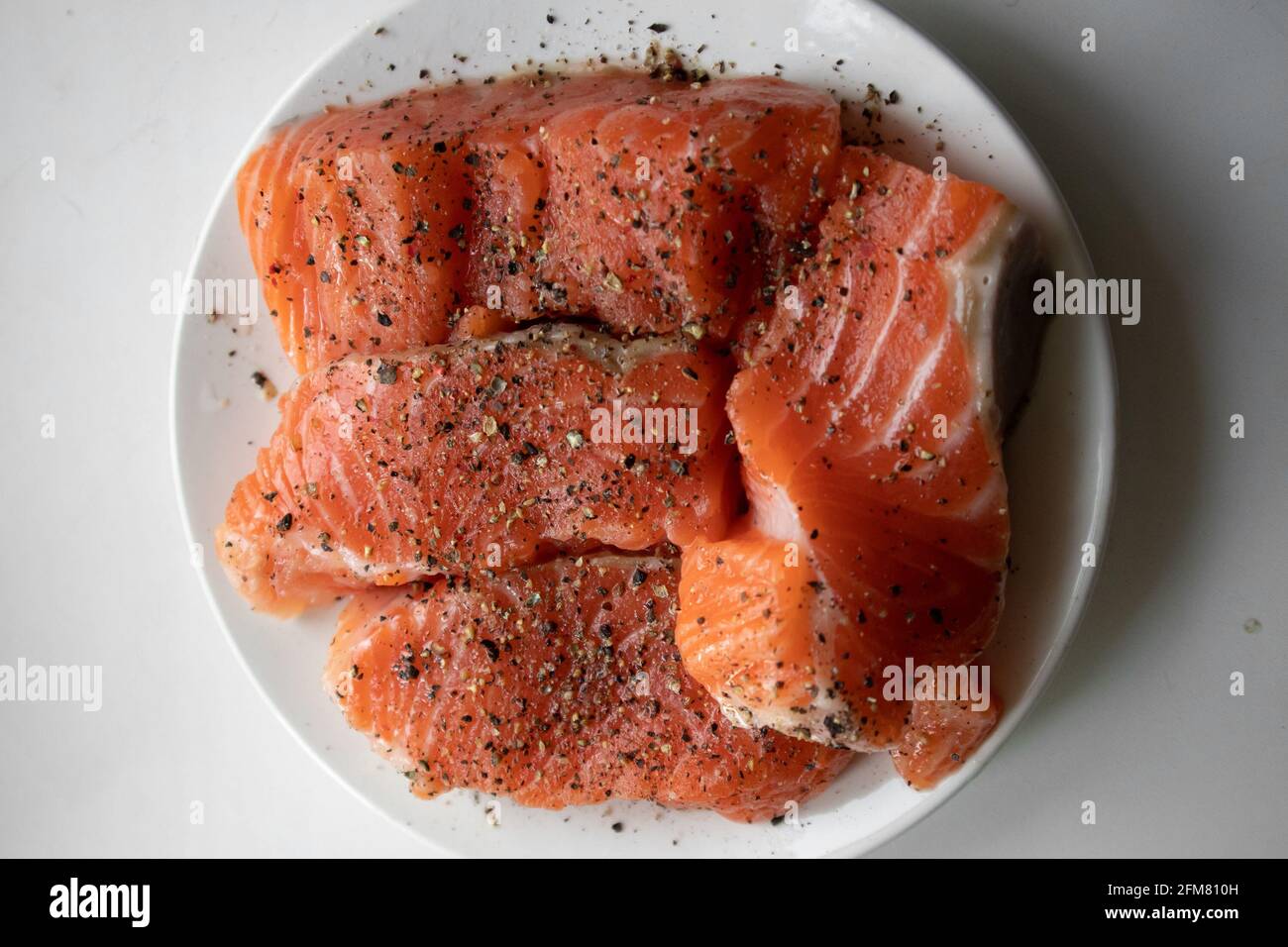 Apetitosos trozos de salmón crudo fresco con especias tumbadas un plato blanco Foto de stock