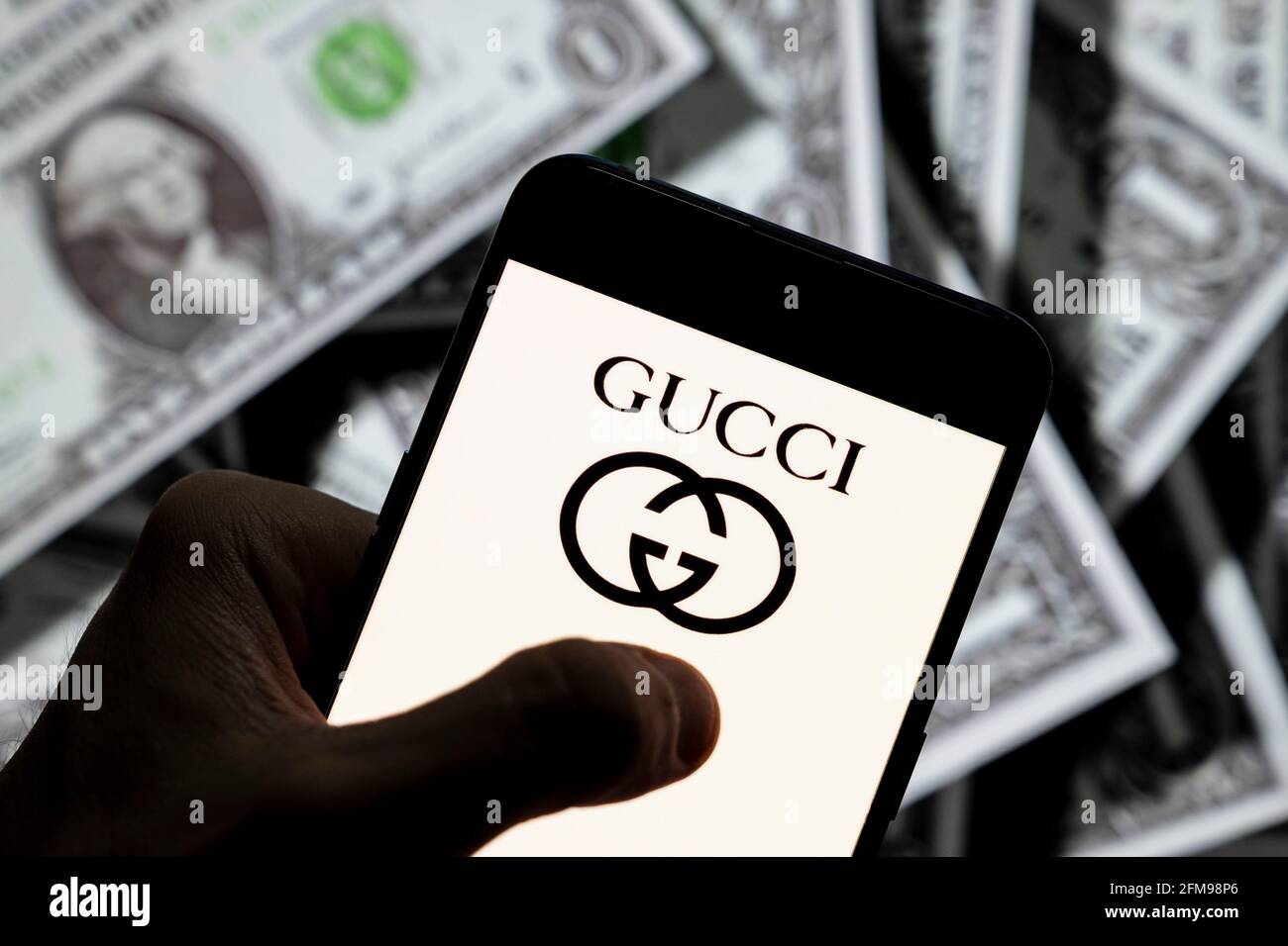 En esta ilustración de la foto, el logotipo de Gucci de la marca italiana de  moda de lujo se muestra en un smartphone con una moneda de fondo en USD  (dólares de