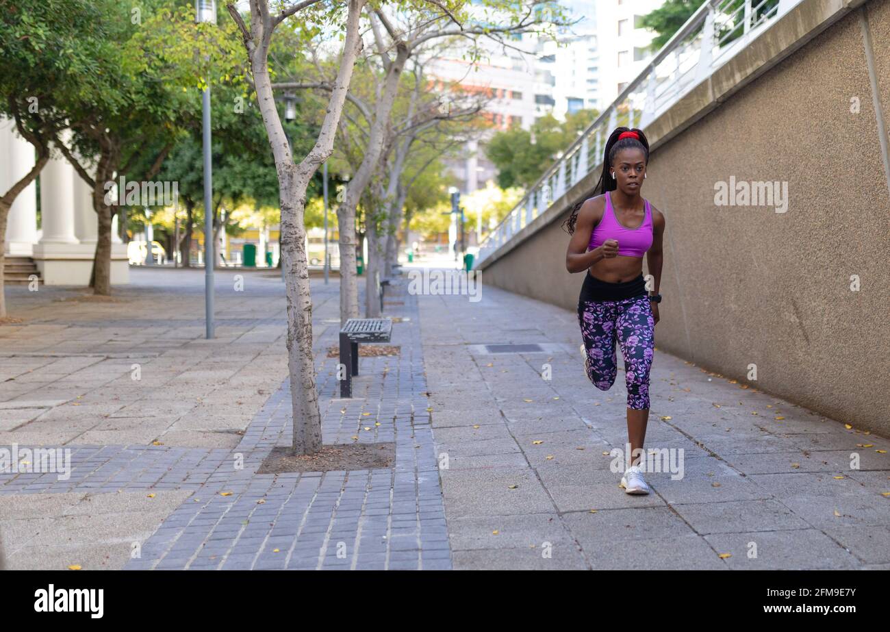 Se adapta a una mujer afroamericana corriendo con auriculares inalámbricos  haciendo ejercicio ciudad Fotografía de stock - Alamy