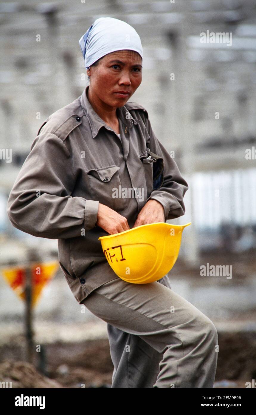 Una trabajadora de la construcción ajusta su casco en un gran lugar de construcción para un asentamiento industrial en las afueras de Hanoi. 04/1994 - Christoph Kel Foto de stock