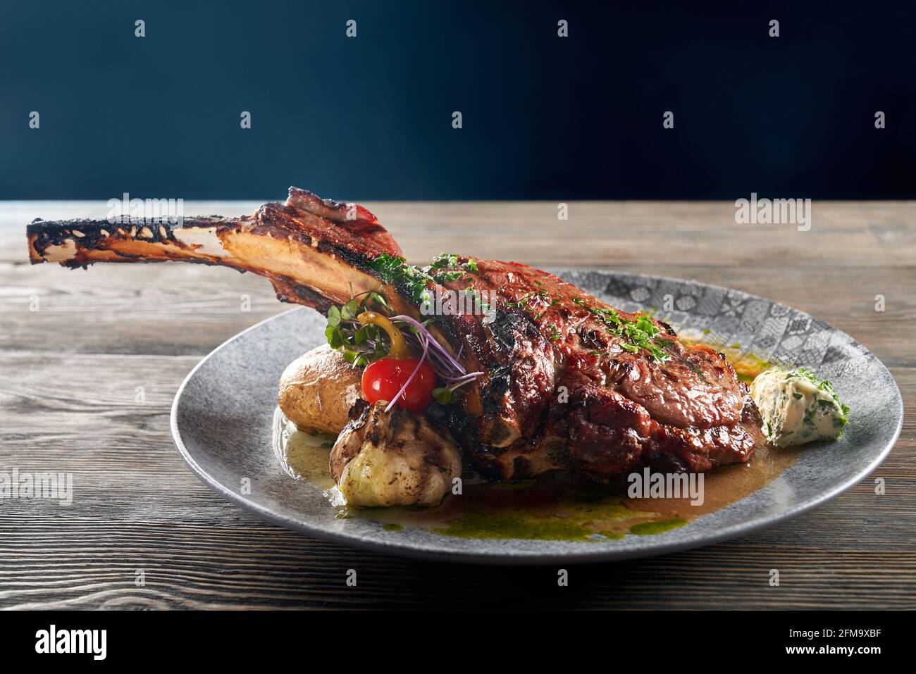 Primer plano de la cocina francesa moderna. Jugoso cordero asado a la  barbacoa sobre hueso servido con ajo, queso, verduras y salsa. Cena aislada  en mesa de woden en el restaurante. Concepto
