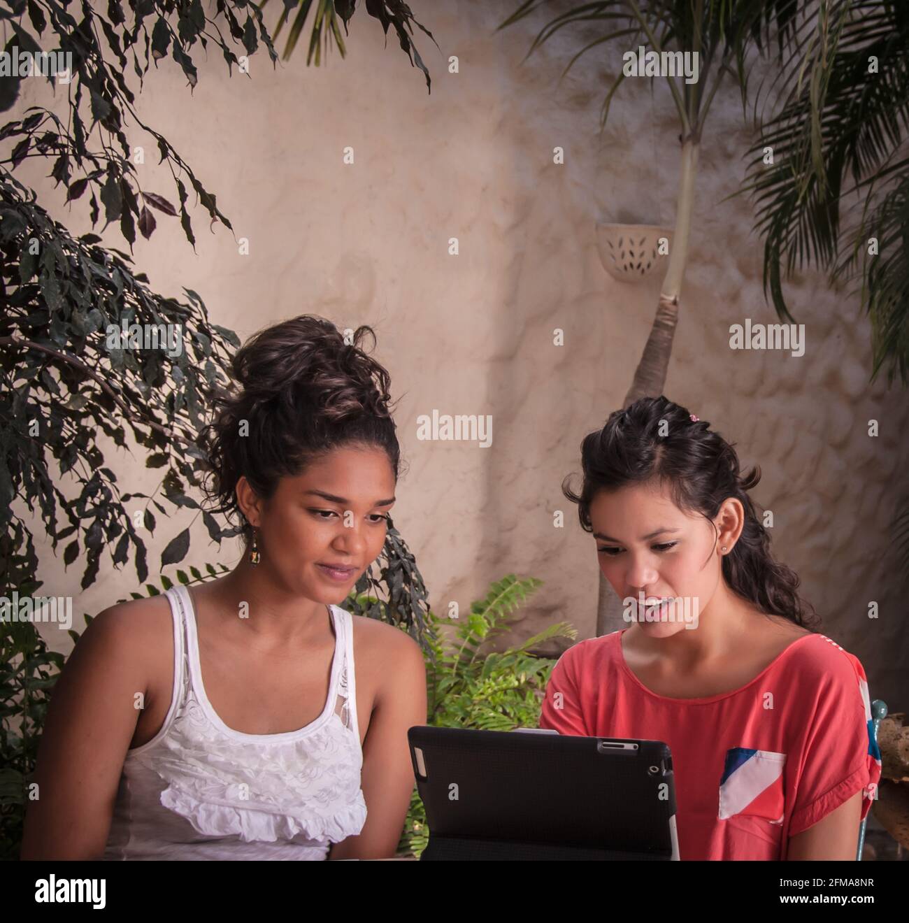 2 jóvenes hispanas usan computadora portátil en el patio tropical de Casa Amorita B&B, Puerto Vallarta en Bahía de Banderas, Jalisco, México. #613PV Foto de stock