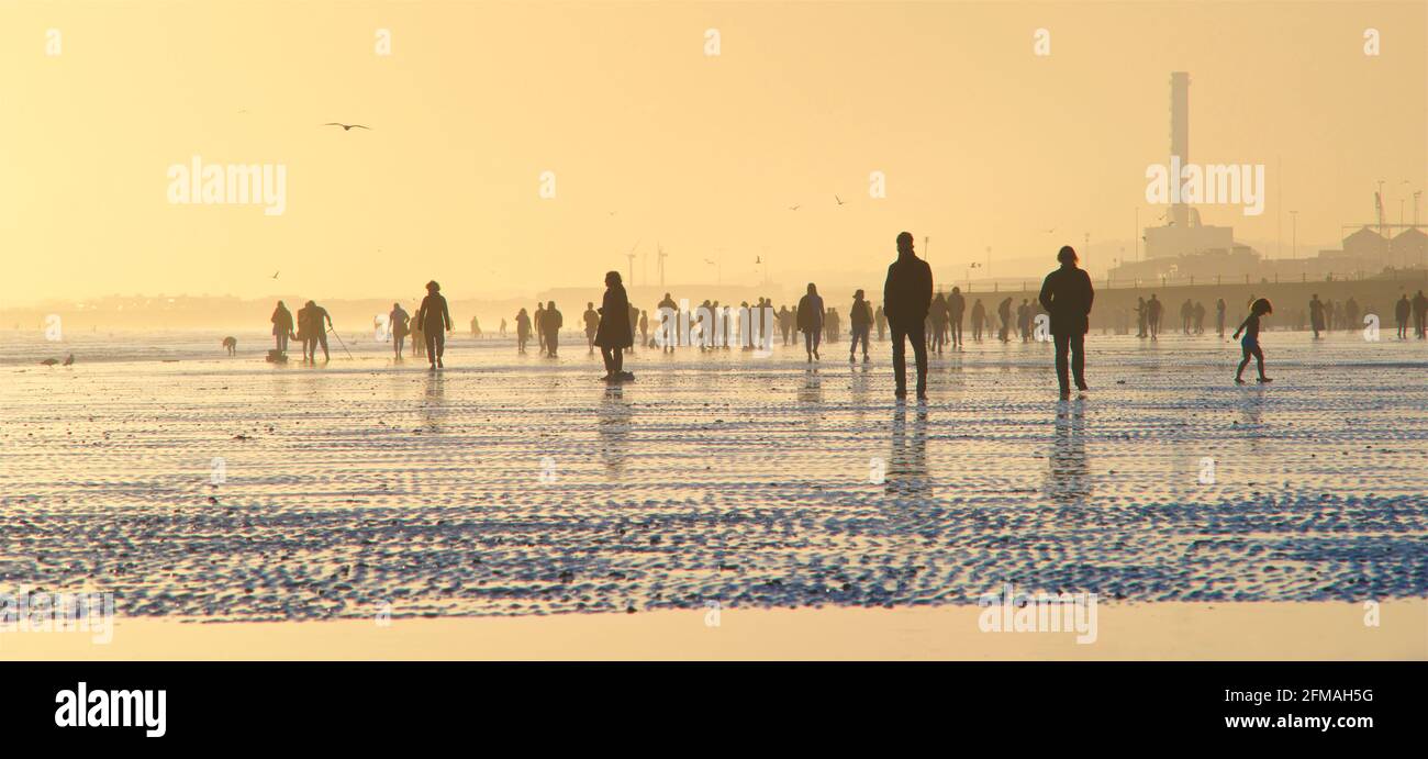 Brighton y Hove playa en la marea baja mirando hacia el oeste. Siluetas de personas caminando a lo largo de la orilla al atardecer. East Sussex, Inglaterra. Remniscent de una pintura de Lowry Foto de stock