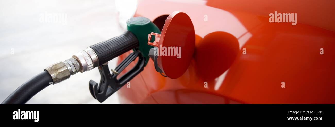 Cierre la puerta del depósito de combustible de forma circular del coche deportivo naranja, mientras se llena con la boquilla verde de la bomba de gas benceno. Foto de stock