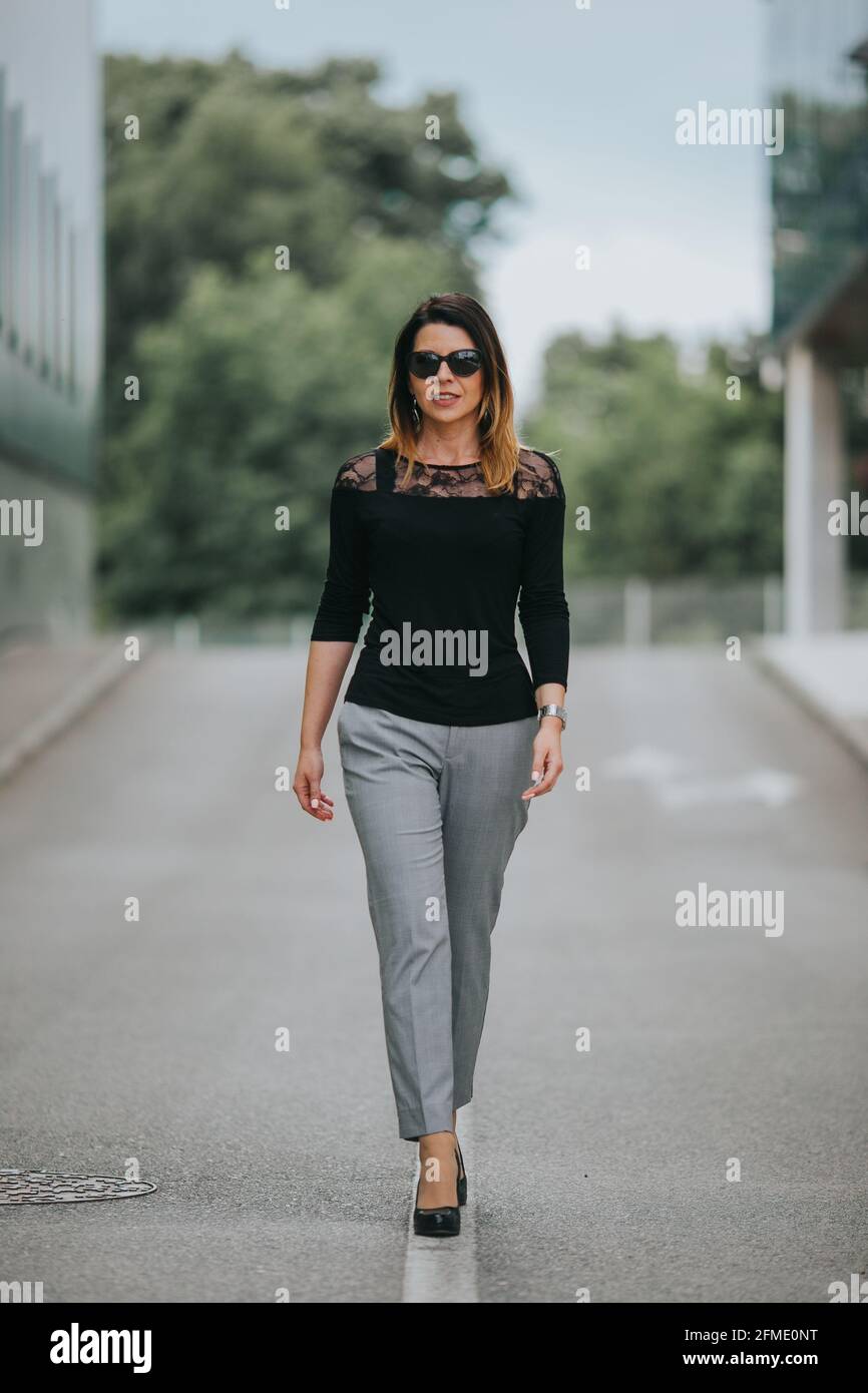 Moderna mujer caucásica con gafas de sol con camisa negra y gris pantalones  caminando en una calle Fotografía de stock - Alamy