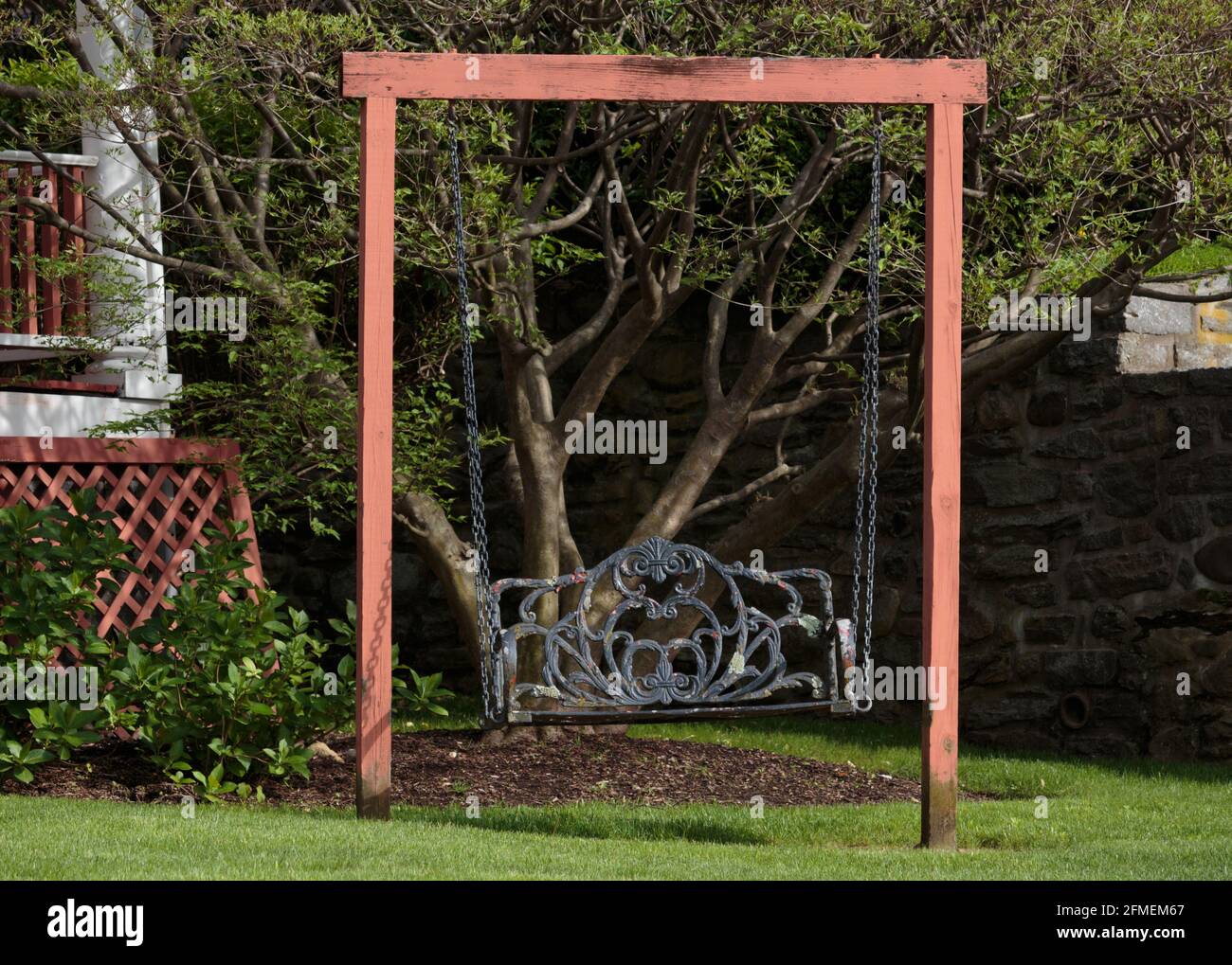un columpio ornamentado, envejecido, de hierro forjado en un pintoresco patio delantero con césped verde, idealista y pintoresco Foto de stock