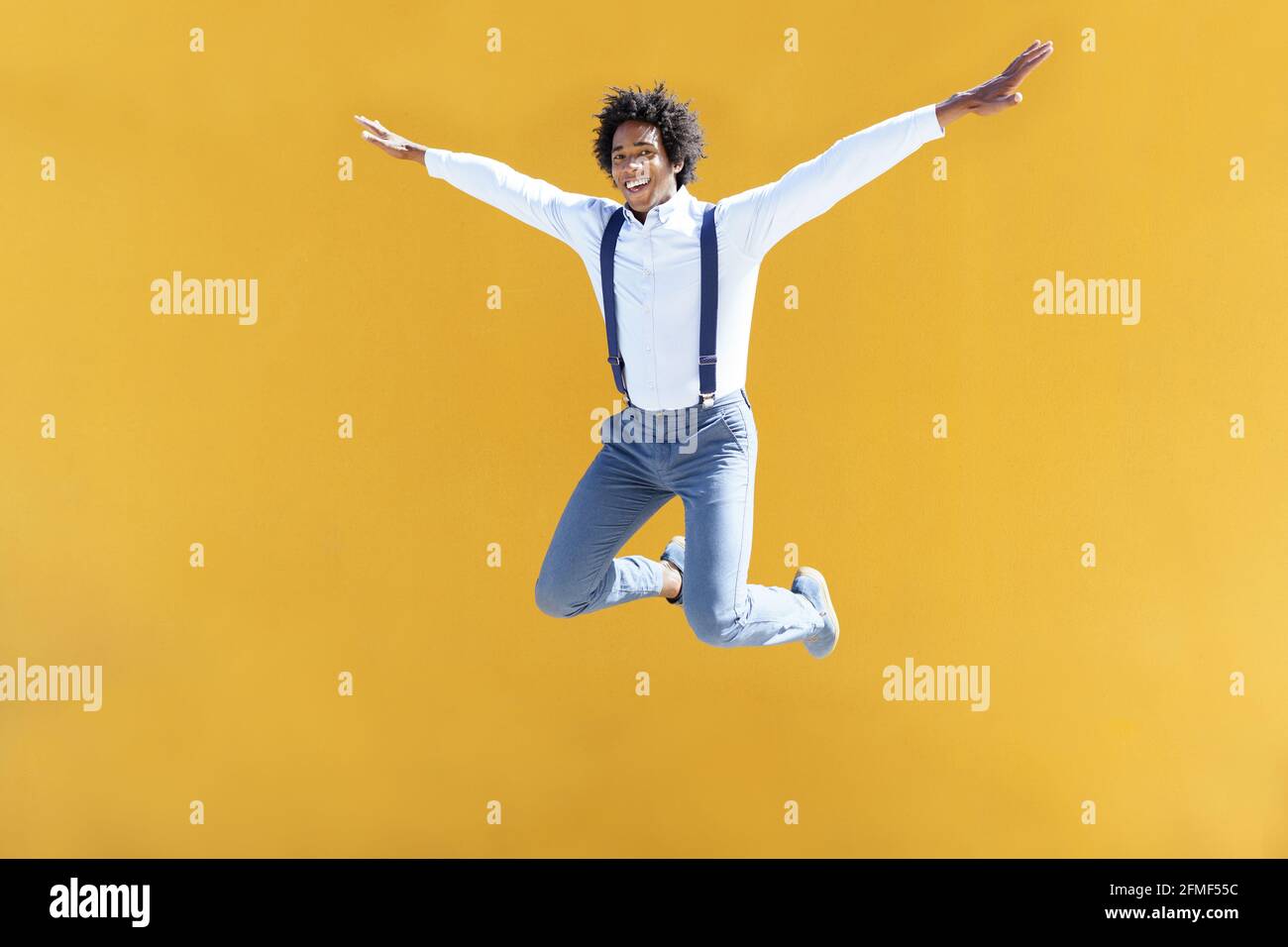 Hombre negro con pelo afro saltando en una ciudad amarilla antecedentes Foto de stock