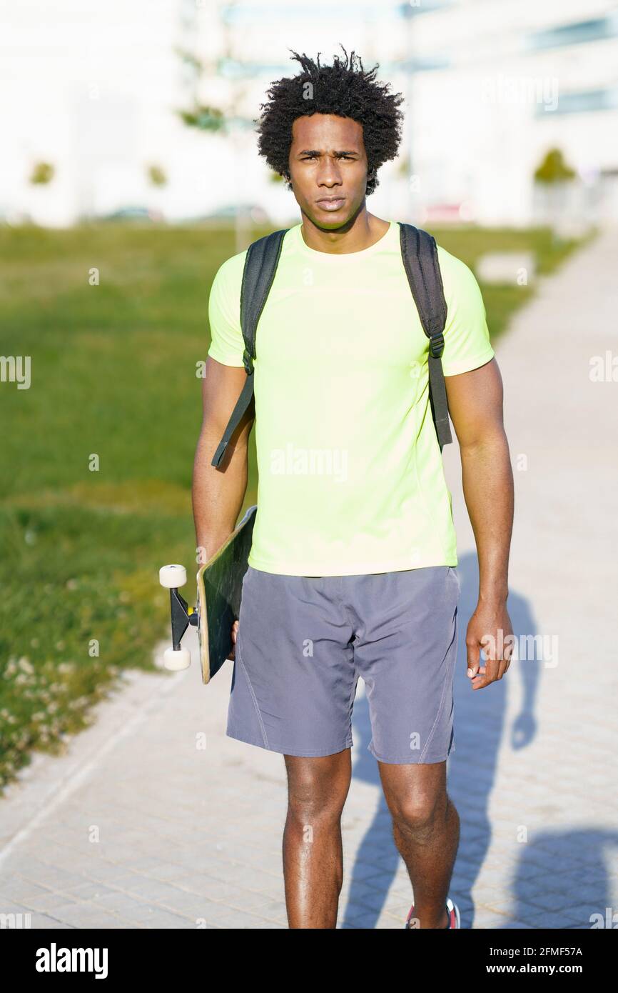 Hombre negro que va para un entrenamiento en ropa deportiva y un skateboard. Foto de stock