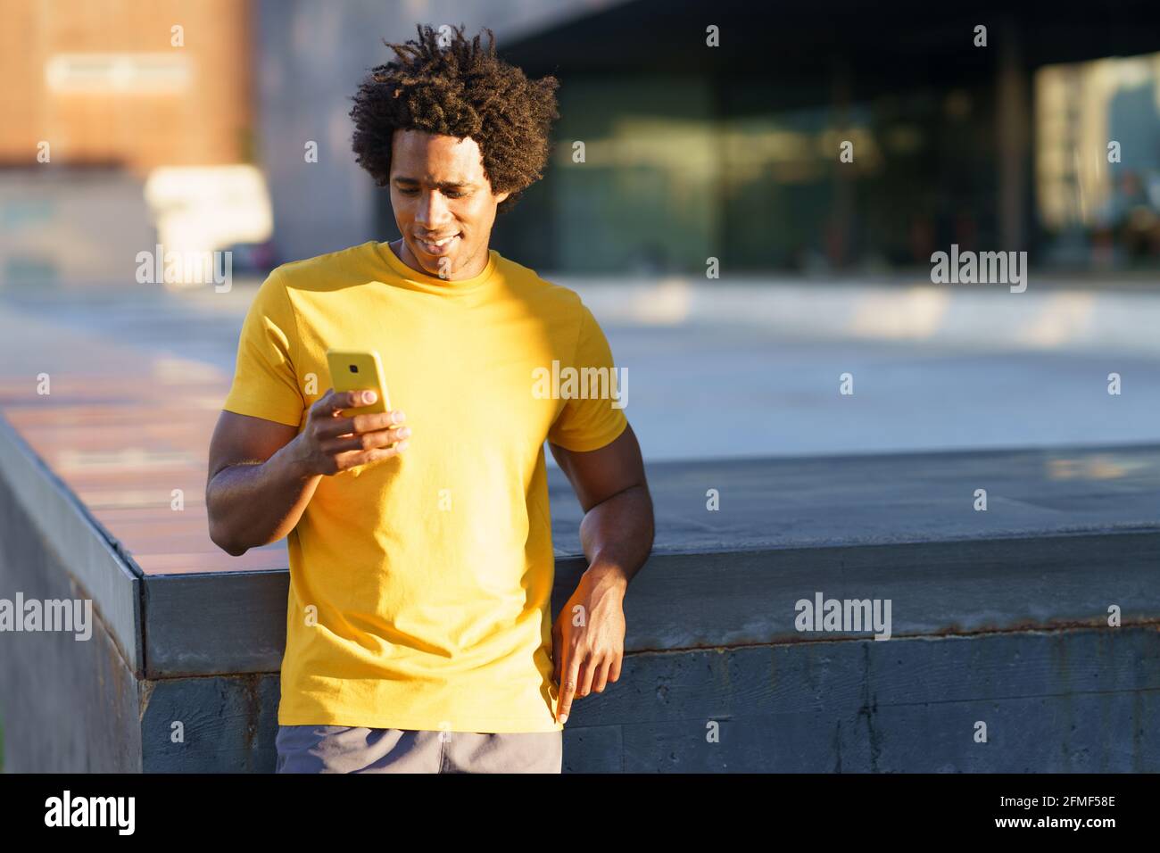 Hombre negro consultando su smartphone mientras descansa de su entrenamiento. Foto de stock