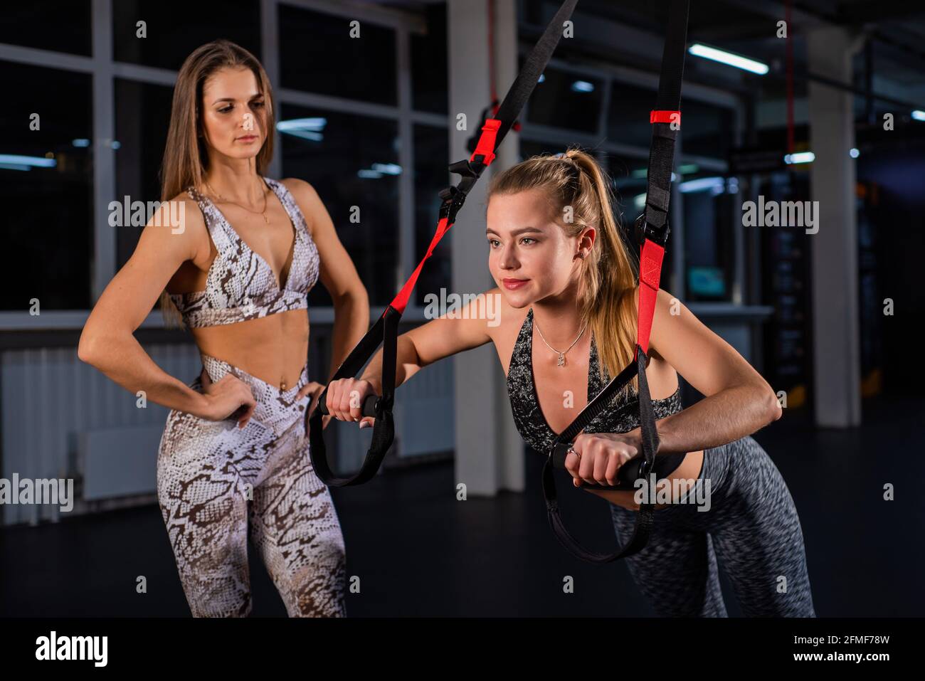 Mujeres haciendo Empuje Brazos de entrenamiento con correas. Formación personal. Una mujer entrenadora en el gimnasio para entrenamiento circular supervisa el correcto Foto de stock