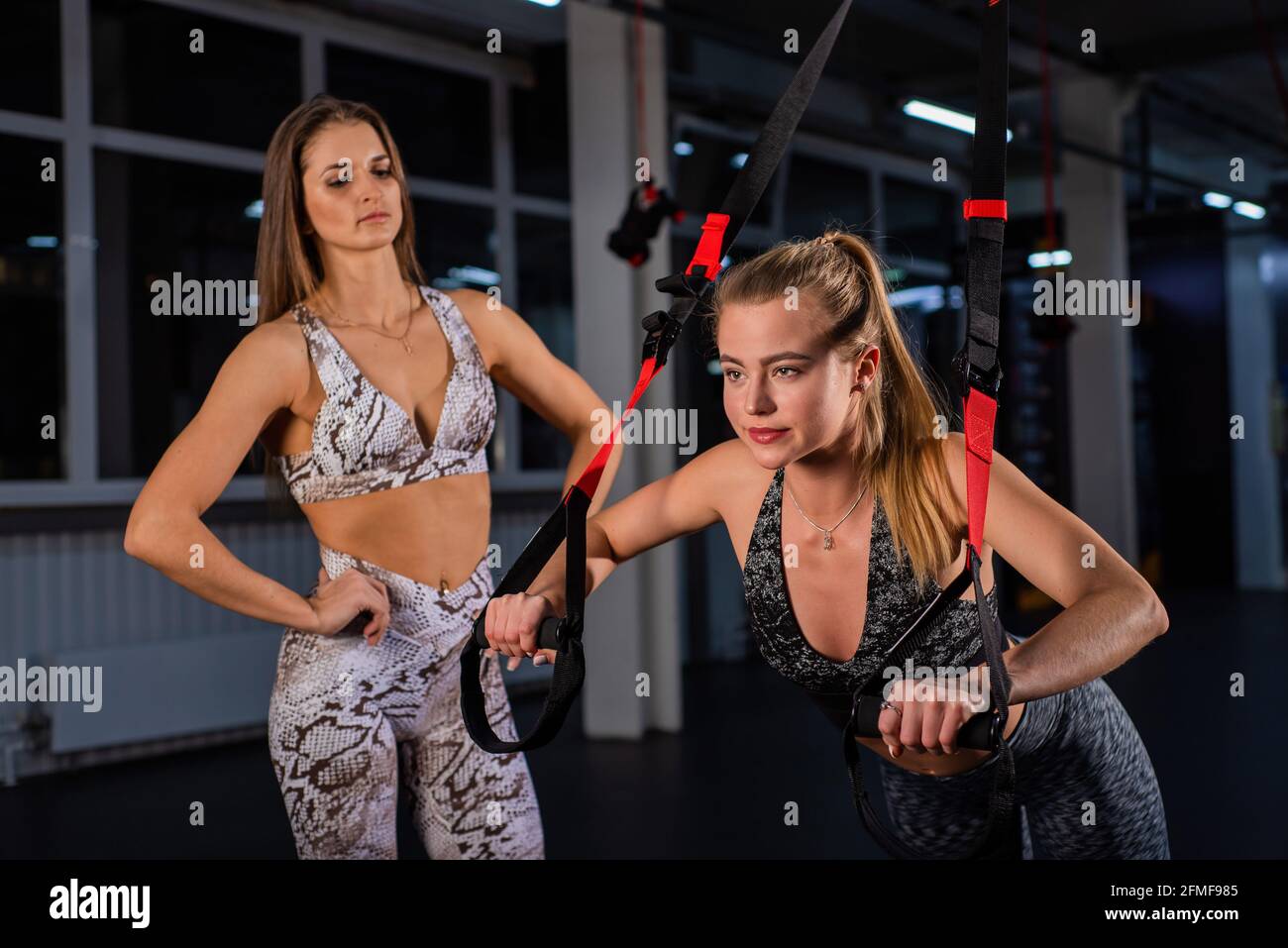 Mujeres haciendo Empuje Brazos de entrenamiento con correas. Formación personal. Una mujer entrenadora en el gimnasio para entrenamiento circular supervisa el correcto Foto de stock