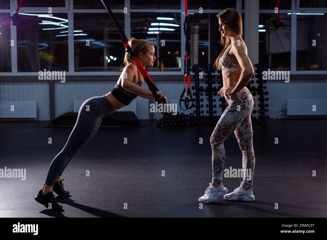 Mujeres haciendo Empuje Brazos de entrenamiento con correas. Formación personal. Una mujer entrenadora en el gimnasio para entrenamiento circular supervisa el correcto Foto de stock