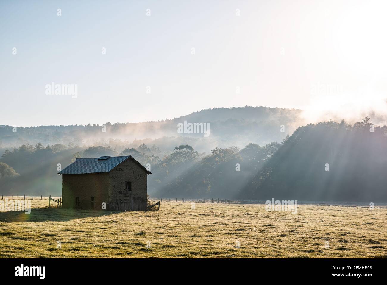 Silueta de la mañana del amanecer del granero de almacenamiento de ladrillo abandonado agrícola En otoño paisaje campo de granja en la campiña rural de Occidente Virginia con Foto de stock