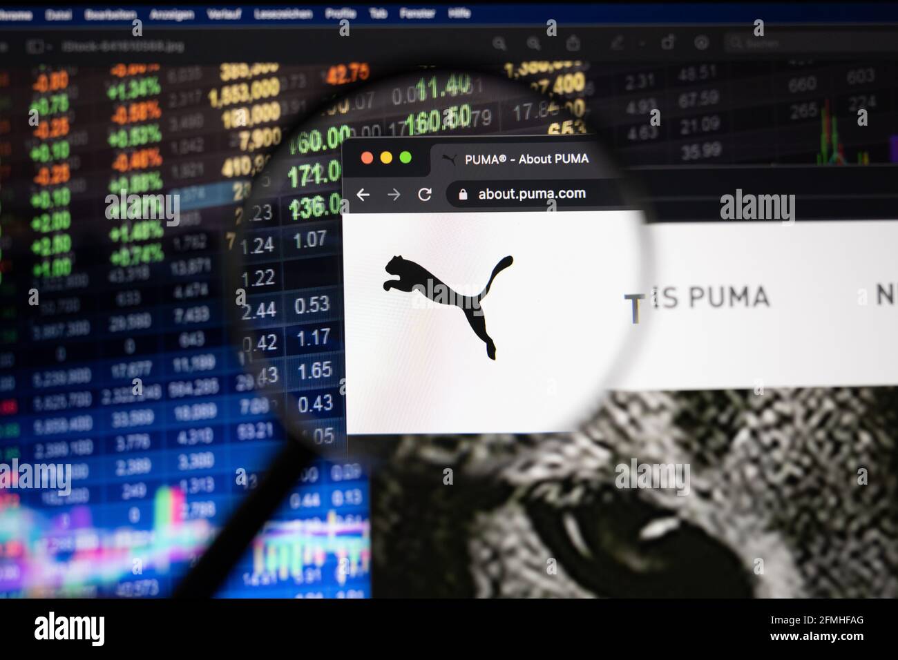 El logotipo de la empresa Puma en un sitio web con una evolución borrosa  del mercado de valores en segundo plano, visto en una pantalla de ordenador  a través de una lupa