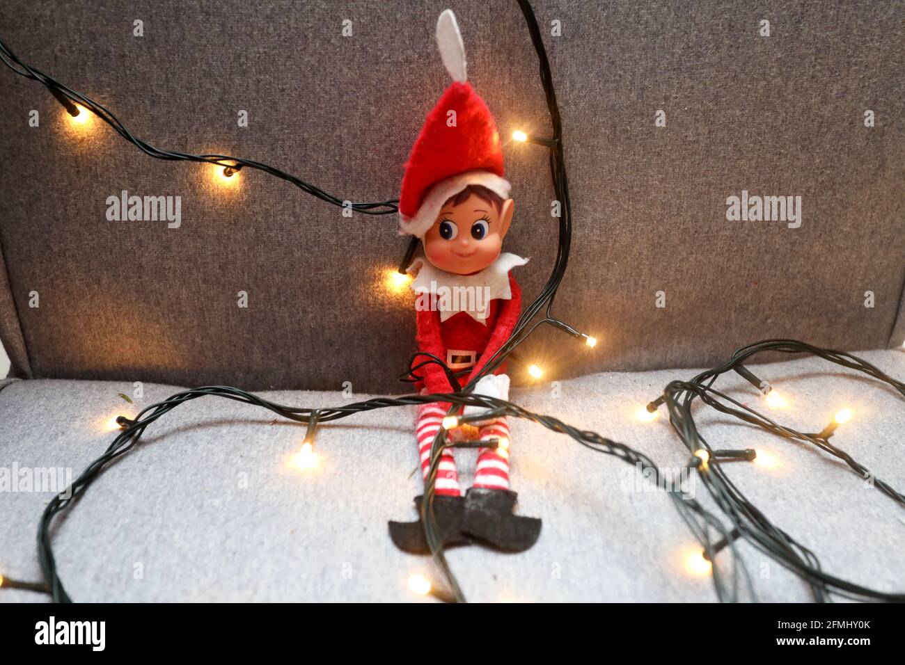 Un elfo en el estante envuelto en luces de Navidad en una silla en West Sussex, Reino Unido. Foto de stock
