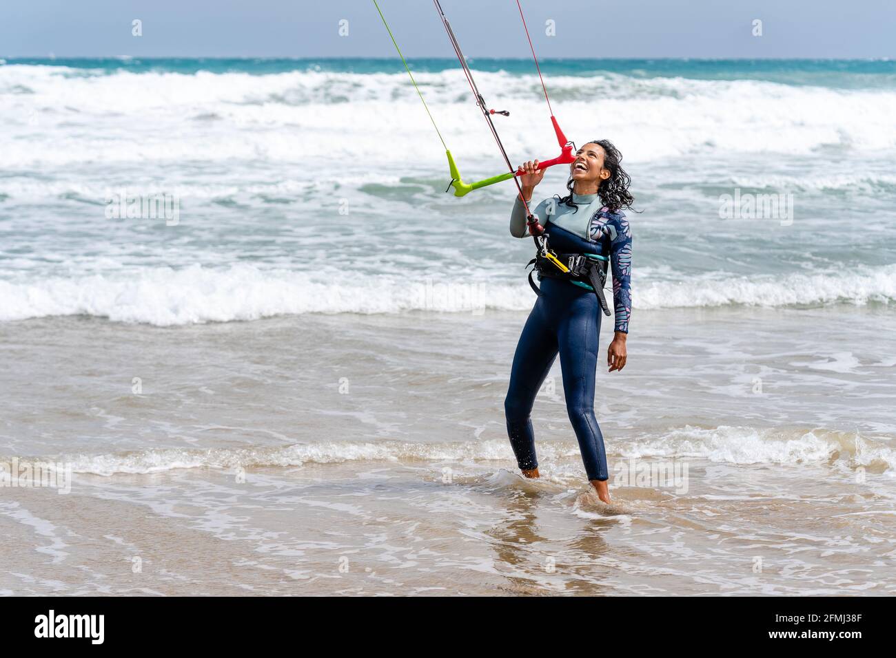Mujer atleta en traje de neopreno con barra de control mirando hacia fuera  orilla arenosa contra el océano espumoso después de practicar kiteboarding  Fotografía de stock - Alamy