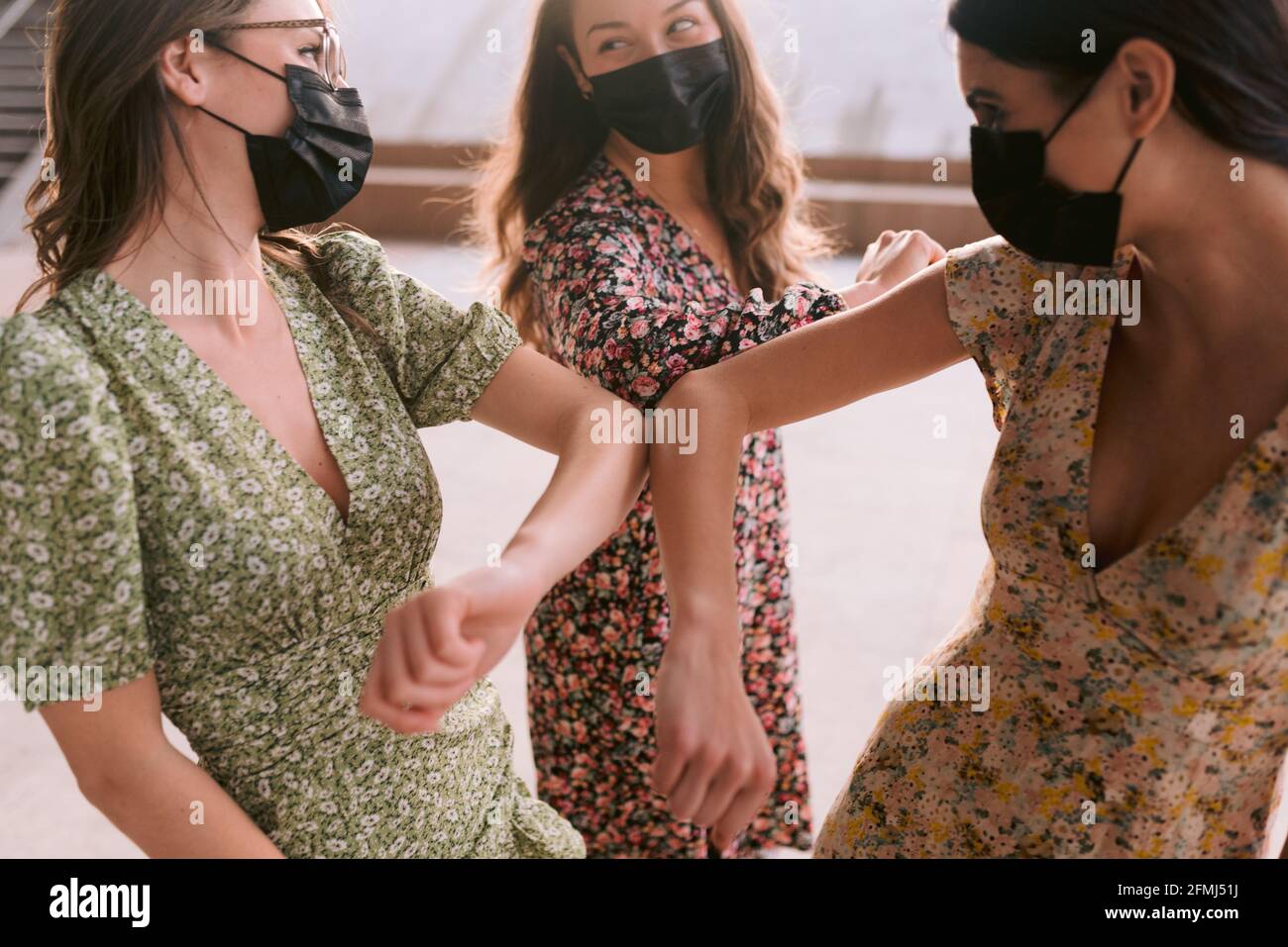 Contenido mejores amigas femeninas en vestidos ornamentales y cara de tela  máscaras tocando los codos mientras se miran unos a otros en la ciudad  durante la pandemia de coronavirus Fotografía de stock -