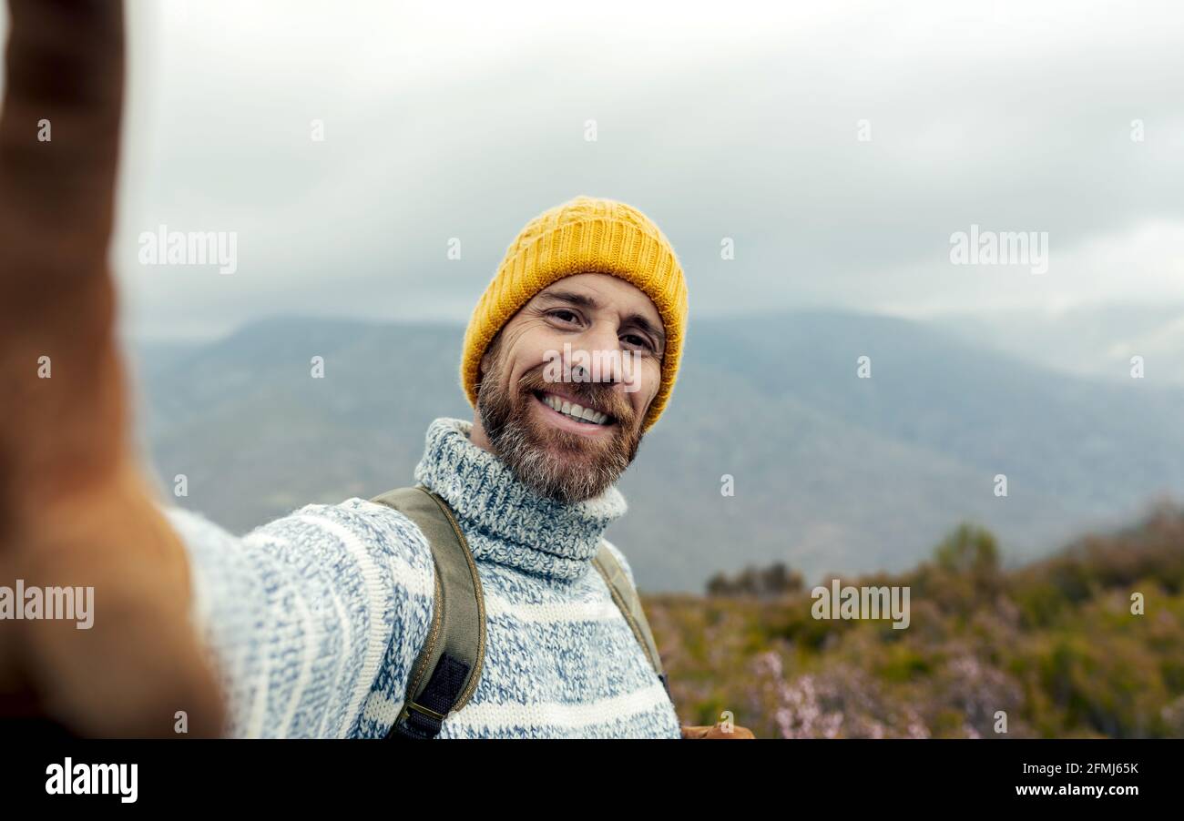 alegre explorador de hombre con barba, mochila y ropa de abrigo tomando  selfie en las montañas y sonriendo con la cámara Fotografía de stock - Alamy