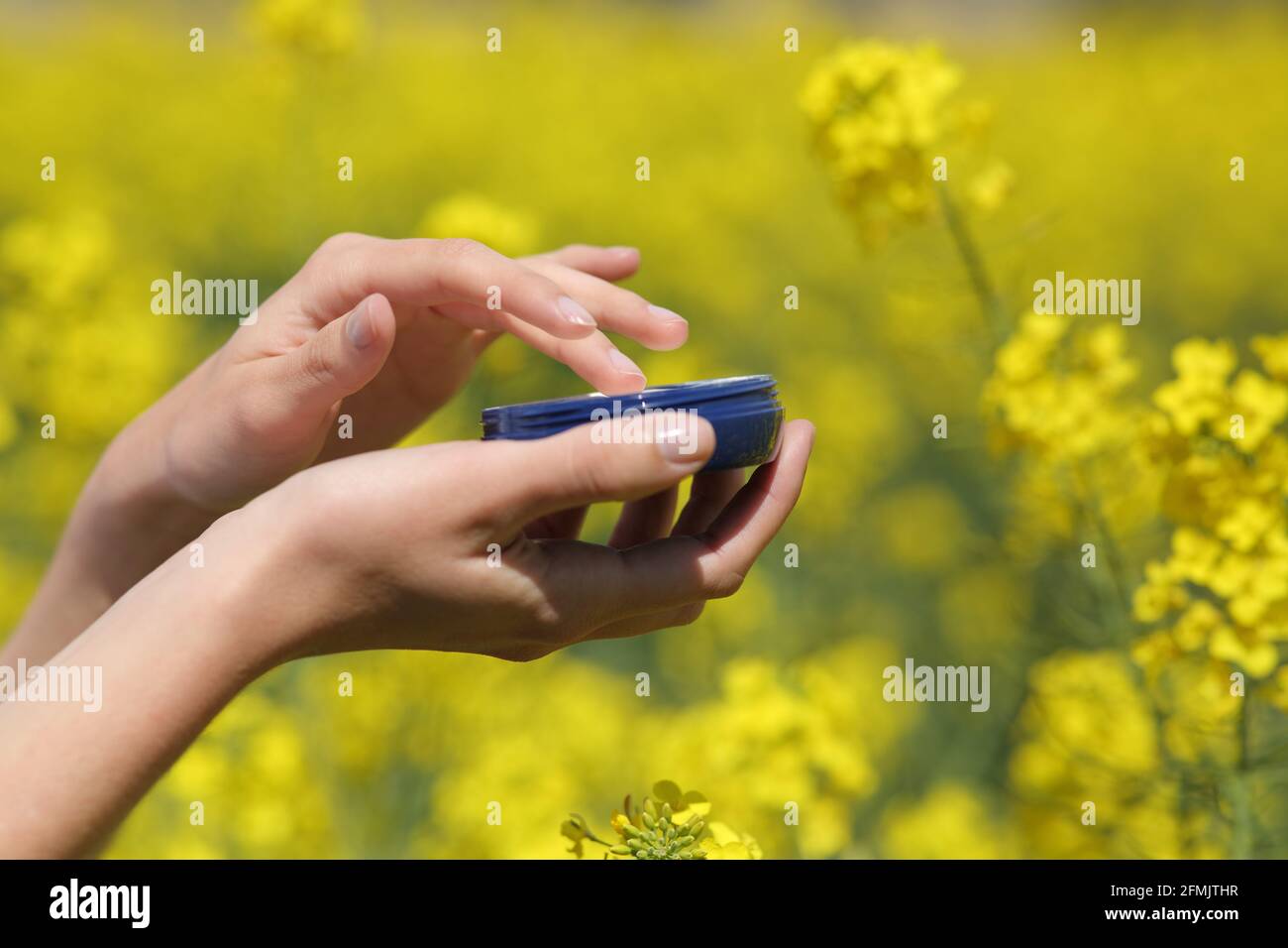 Primer plano de una mano de mujer que sostiene la jarra hidratante en un campo amarillo en la temporada de primavera Foto de stock