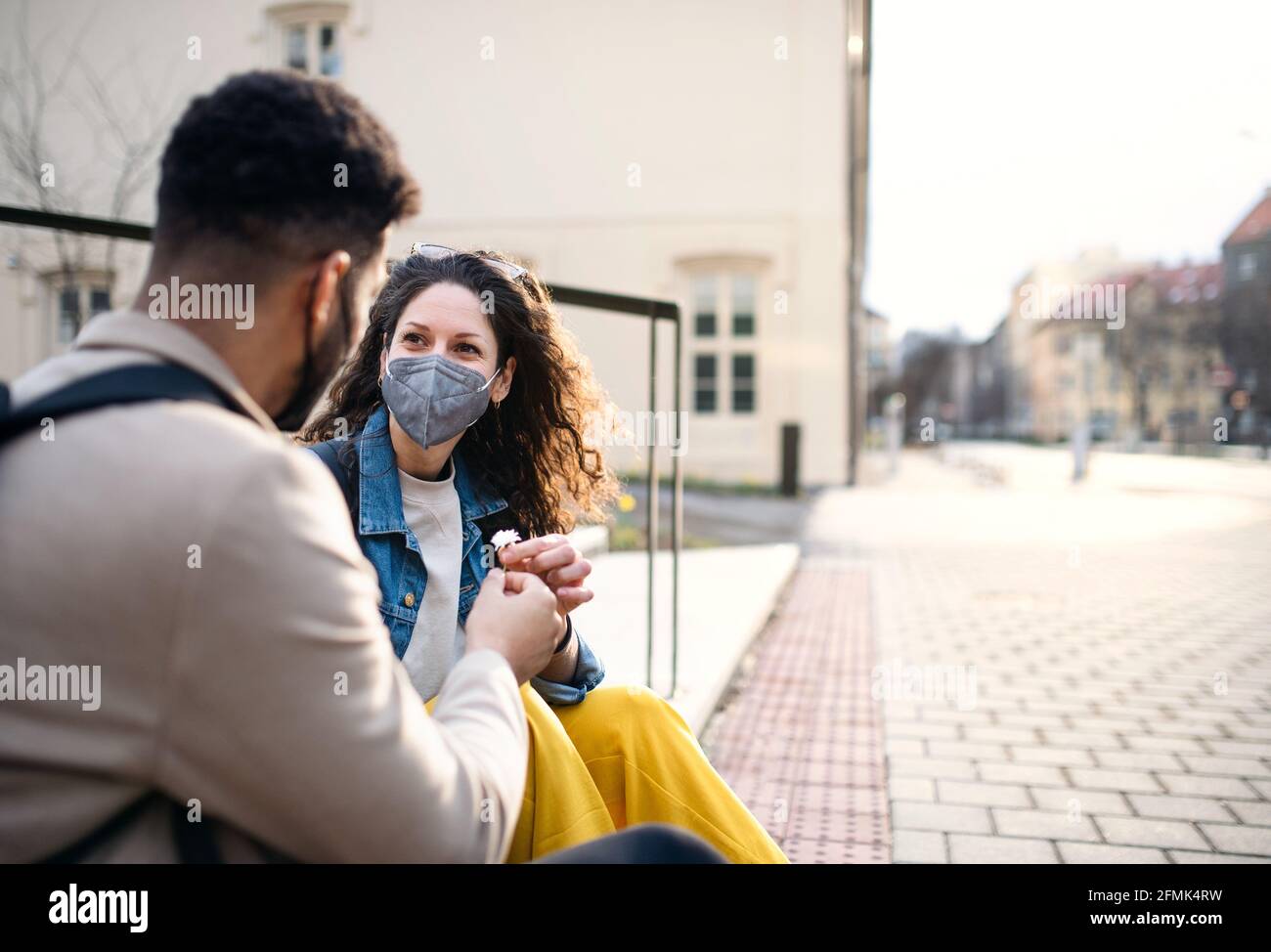 Hombre dando flor a la mujer al aire libre en la ciudad, coronavirus, el amor y de vuelta al concepto normal. Foto de stock