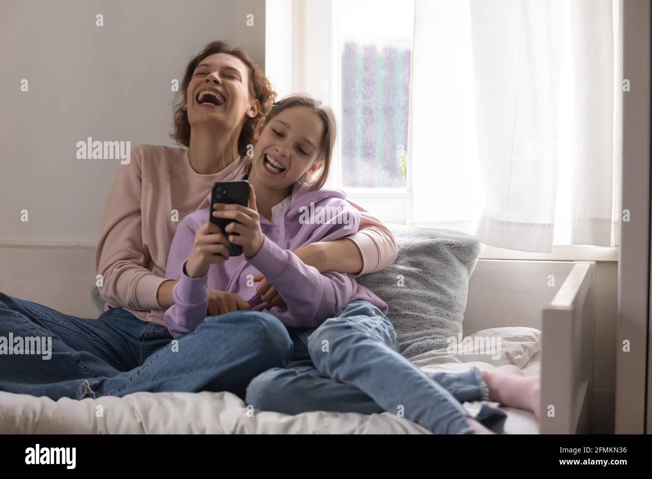 Bonding feliz madre y hija adolescente riendo de vídeo divertido. Foto de stock