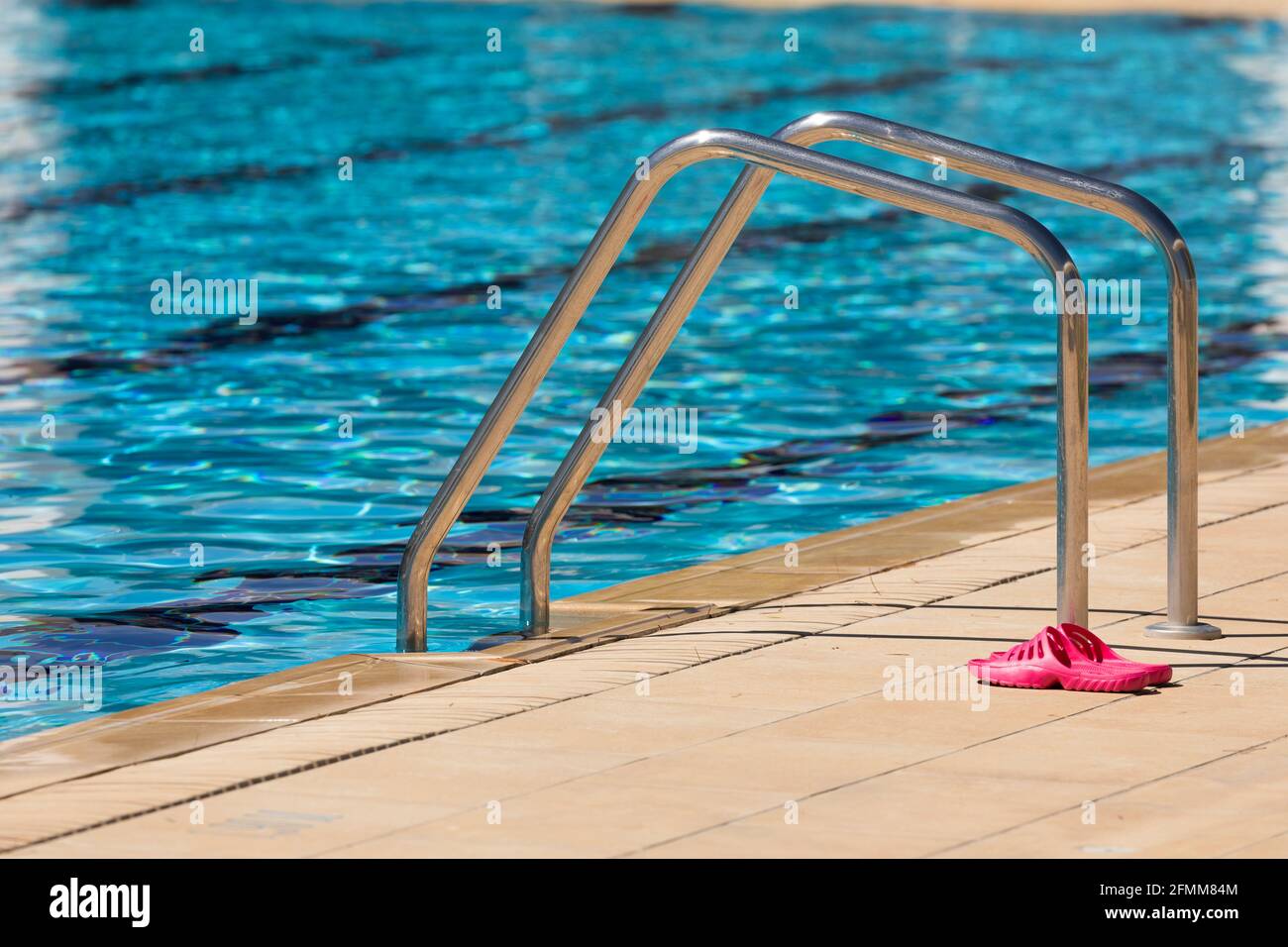Chanclas rosadas, junto a las escaleras de acceso al agua, de acero  inoxidable, situadas al borde de una piscina en el municipio de Gallur,  Arag Fotografía de stock - Alamy