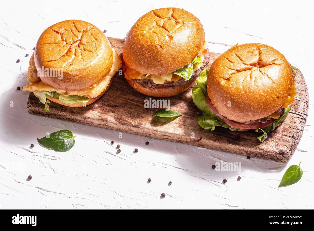 Hamburguesas frescas, comida rápida norteamericana. Surtido de tres piezas,  luz dura moderna, sombra oscura. Tabla de cortar de madera, fondo blanco de  masilla, espacio de copia Fotografía de stock - Alamy