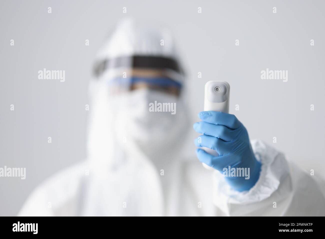 Doctor en traje protector contra la peste y termómetro infrarrojo que sostiene la pantalla primer plano Foto de stock