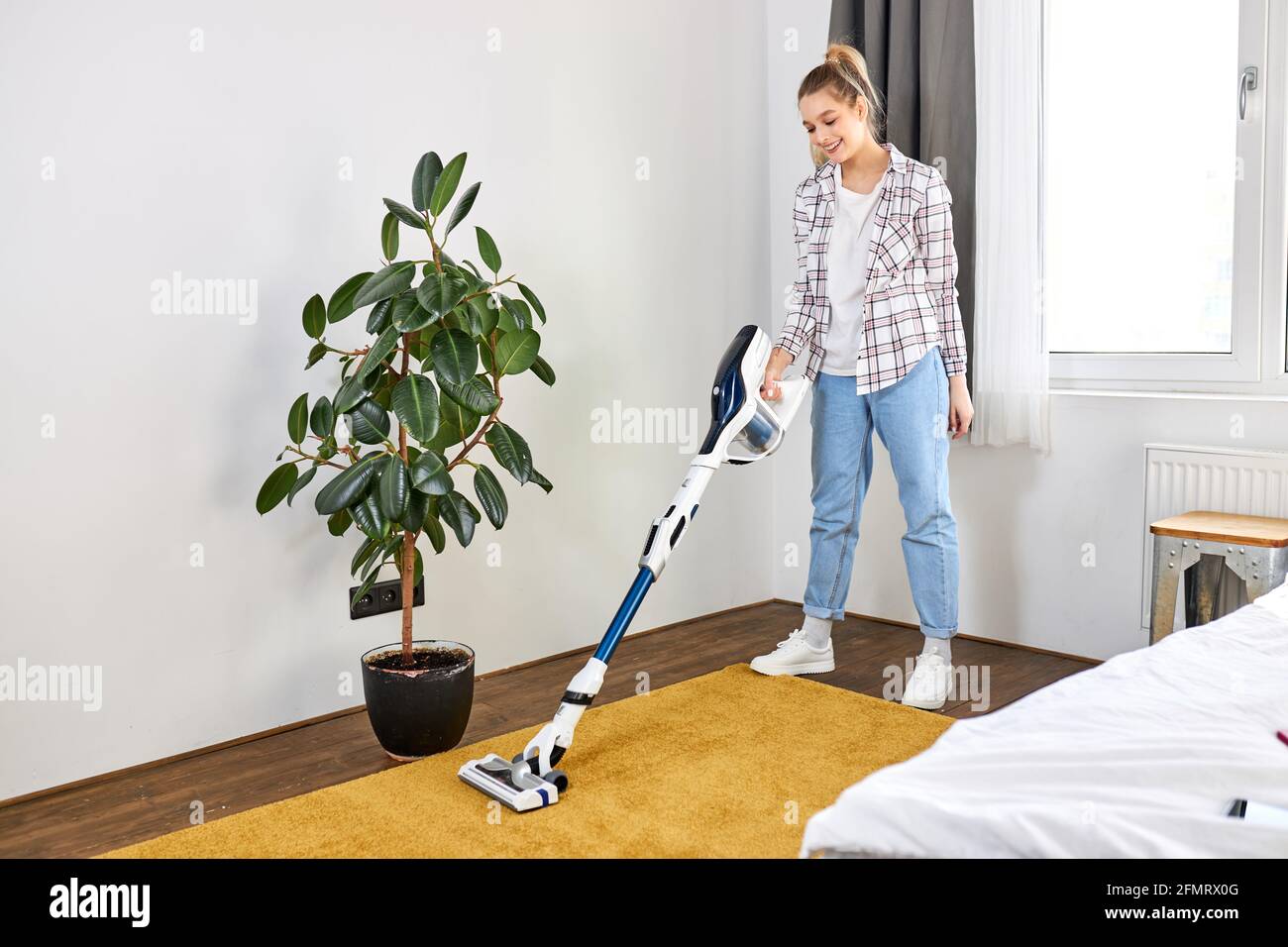 Mujer en el uso casual aspiradora limpieza alfombra amarilla, tidying  blanco moderna sala de estar. Hogar, concepto de limpieza. Vista lateral  Fotografía de stock - Alamy