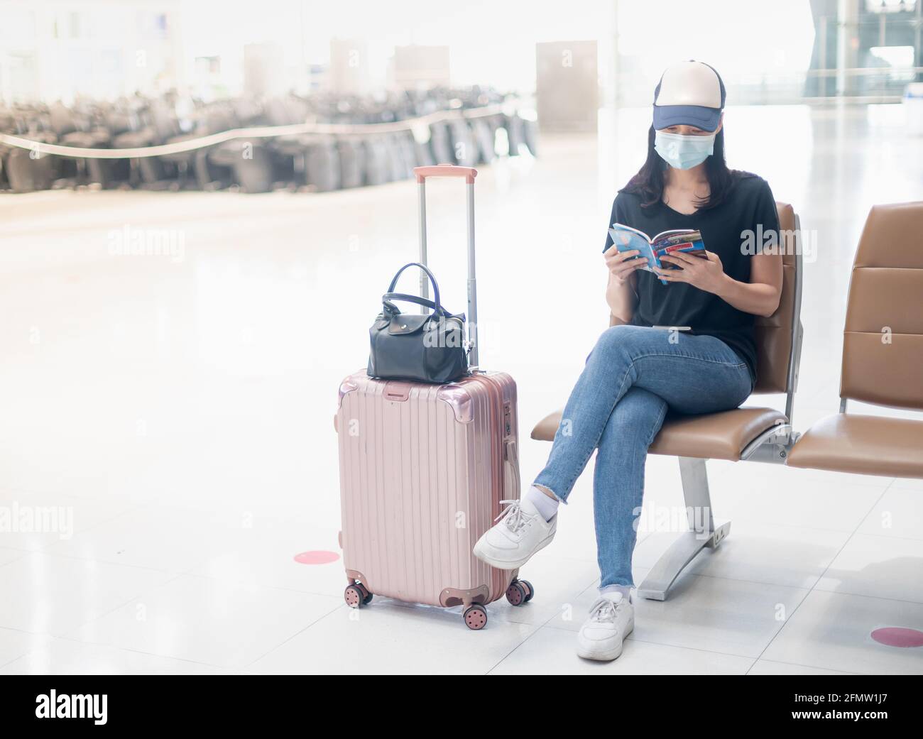 Una chica asiática que lleva una marca quirúrgica con equipaje de mano en  el aeropuerto internacional leyendo un libro mientras espera su vuelo,  durante el Covid Fotografía de stock - Alamy