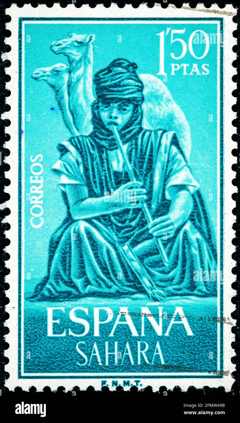 SAHARA ESPAÑOL - ALREDEDOR de 1964: Sello impreso en España. Espectáculo:  Niño sentado en el desierto tocando un instrumento musical de flauta con el  fondo de Fotografía de stock - Alamy