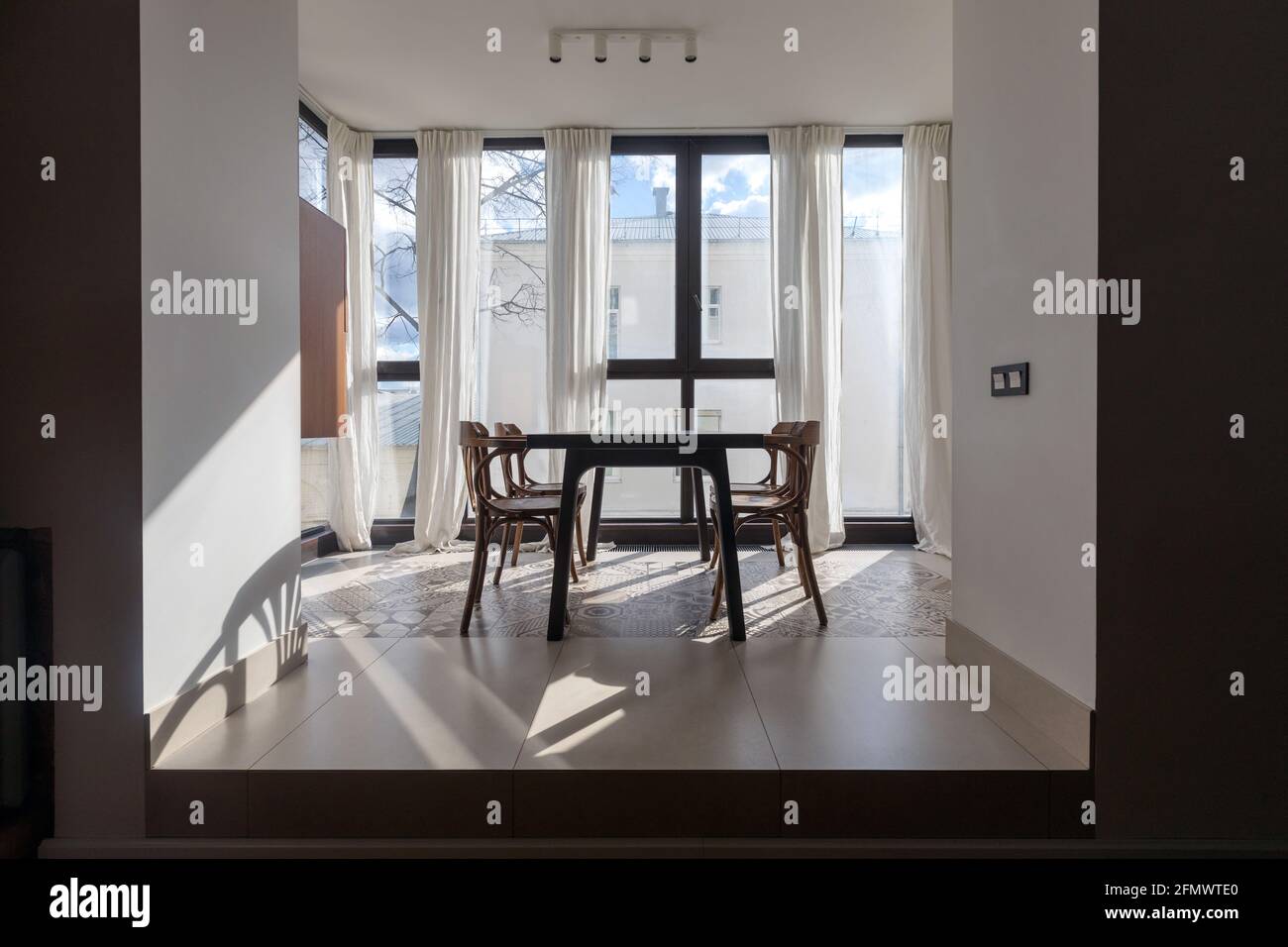 Mesa de comedor y sillas situadas frente a la ventana panorámica apartamento moderno con decoración minimalista, con cortinas blancas diseño interior Foto de stock