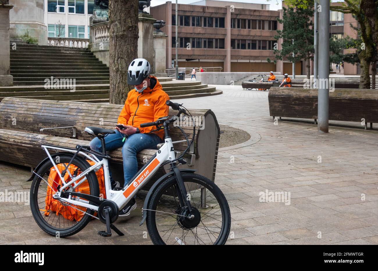 Un hombre de entrega de bicicleta eléctrica justo comer tomando un descanso En el centro de Liverpool Foto de stock