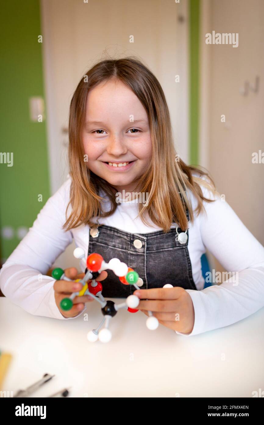 una niña joven peto negro se sienta en su habitación y aprende sobre un modelo para moléculas Fotografía stock - Alamy